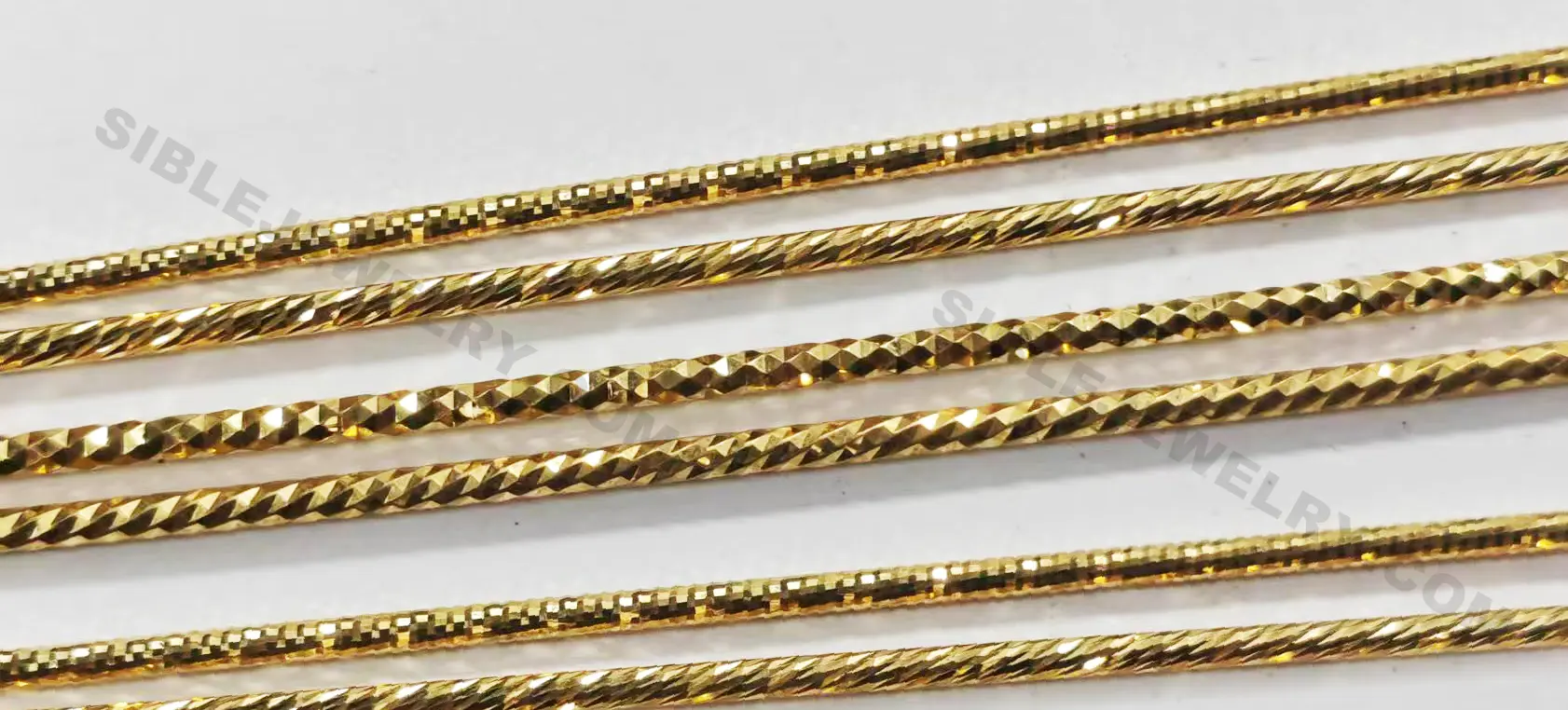 A collection of gold chains with diamond-cut textures in different styles and thicknesses, displayed on a white background.